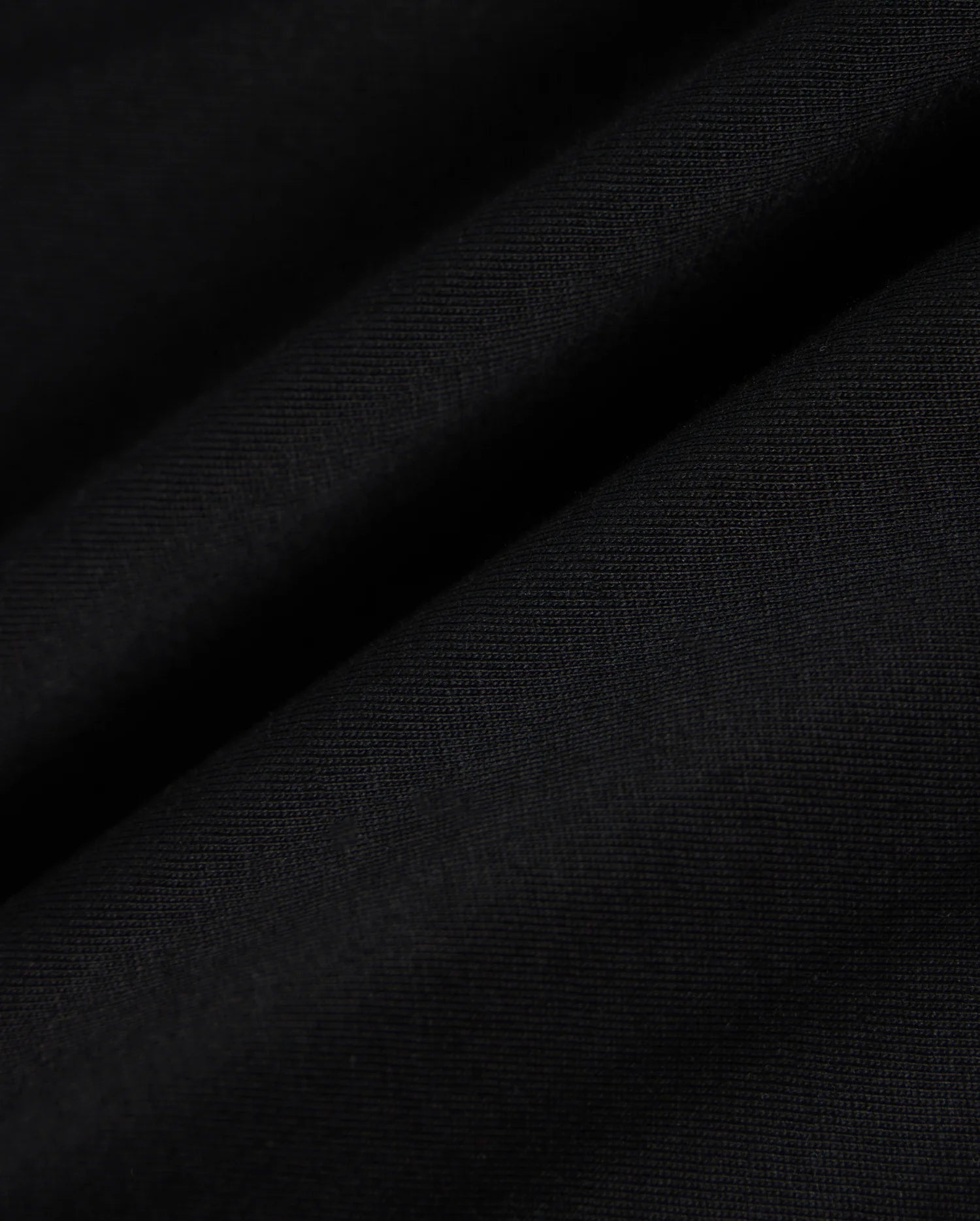 Close-up view of the fabric of the KIDS MALTON GRAPHIC TEE - B0U795D200 by Psycho Bunny, featuring a black hue with a smooth texture and visible fine weave, showcasing subtle diagonal folds and ripples, reminiscent of Peruvian craftsmanship.