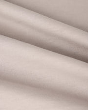 A close-up view of the smooth, beige fabric of the KIDS MALTON GRAPHIC TEE - B0U795D200 from Psycho Bunny shows gentle folds that highlight its soft texture and fine weave. Made from luxurious Pima cotton, the surface appears slightly reflective, creating a subtle play of light and shadow across the material.