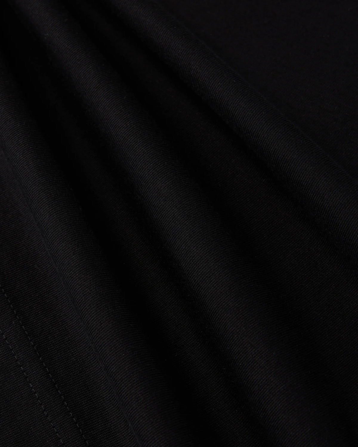 A close-up view of the smooth, dark fabric of the KIDS LOS ANGELES CITY TEE - B0U861A2PC by Psycho Bunny shows a fine, consistent weave. The folds create subtle shadows and highlights, accentuating the texture and soft appearance of this luxurious Peruvian Pima cotton material, suggesting it is well-crafted and of high quality.