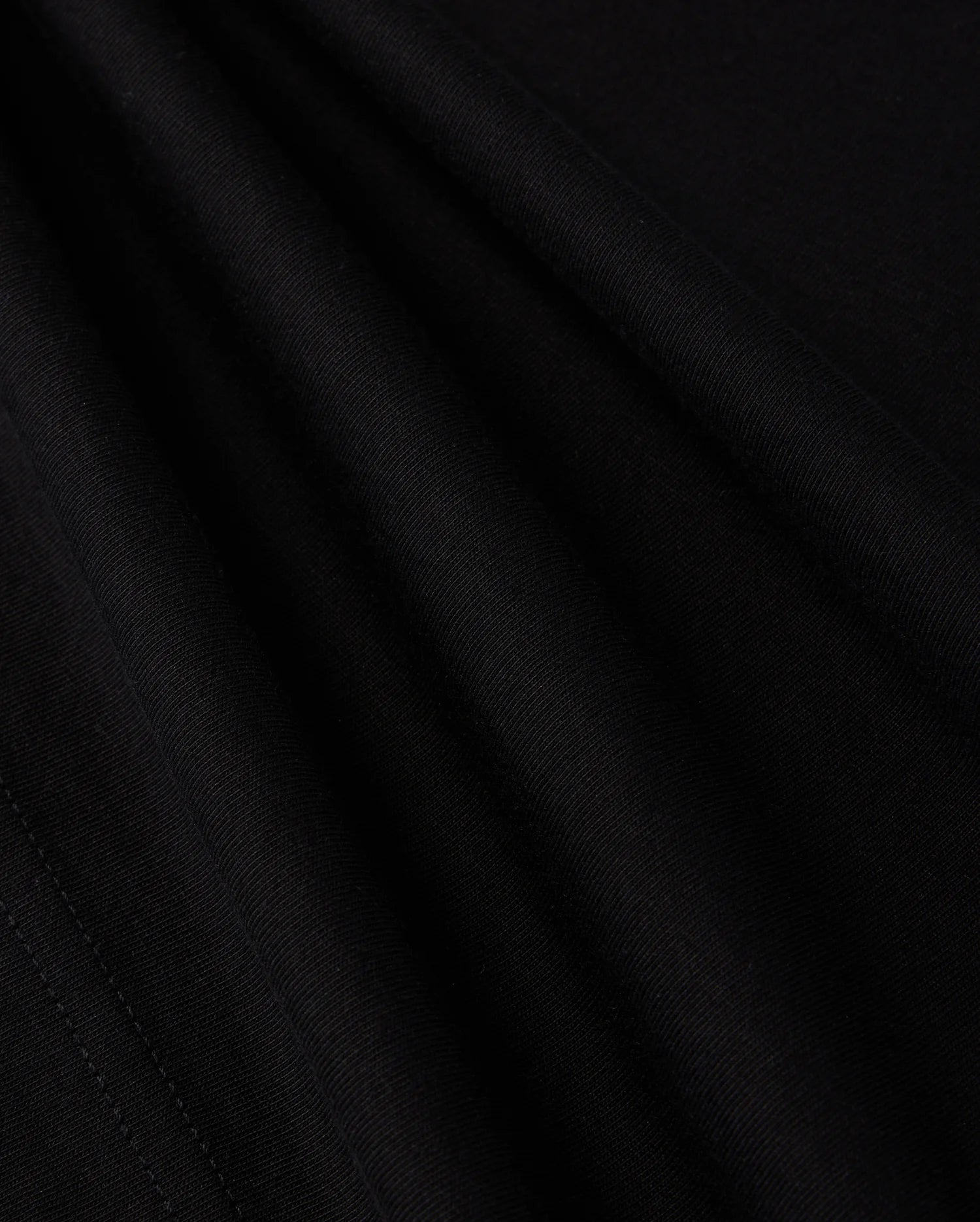 A close-up view of the smooth, dark fabric of the KIDS LOS ANGELES CITY TEE - B0U861A2PC by Psycho Bunny shows a fine, consistent weave. The folds create subtle shadows and highlights, accentuating the texture and soft appearance of this luxurious Peruvian Pima cotton material, suggesting it is well-crafted and of high quality.
