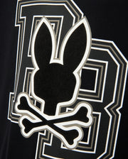 The KIDS ZACK GRAPHIC TEE - B0U897D200 from Psycho Bunny features a black and white design with a Psycho Bunny silhouette above two crossed bones, evoking a skull and crossbones theme, accompanied by a stylized letter "B" in the background. Made from soft Pima cotton, this tee is a striking statement piece.