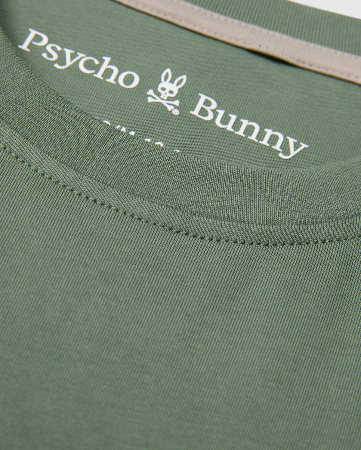 Close-up of a KIDS ZACK GRAPHIC TEE in green, made from luxurious Pima cotton by Psycho Bunny, featuring the iconic bunny and crossbones logo printed on the inner neckline.