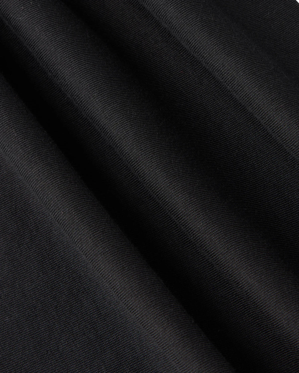 Experience a close-up view of the black Pima cotton fabric featured in the KIDS TACOMA GRAPHIC TEE - B0U909D200 by Psycho Bunny, showcasing a subtle diagonal texture that creates a smooth, elegant surface. The folds of the tee suggest movement and depth, hinting at exquisite embroidered details.