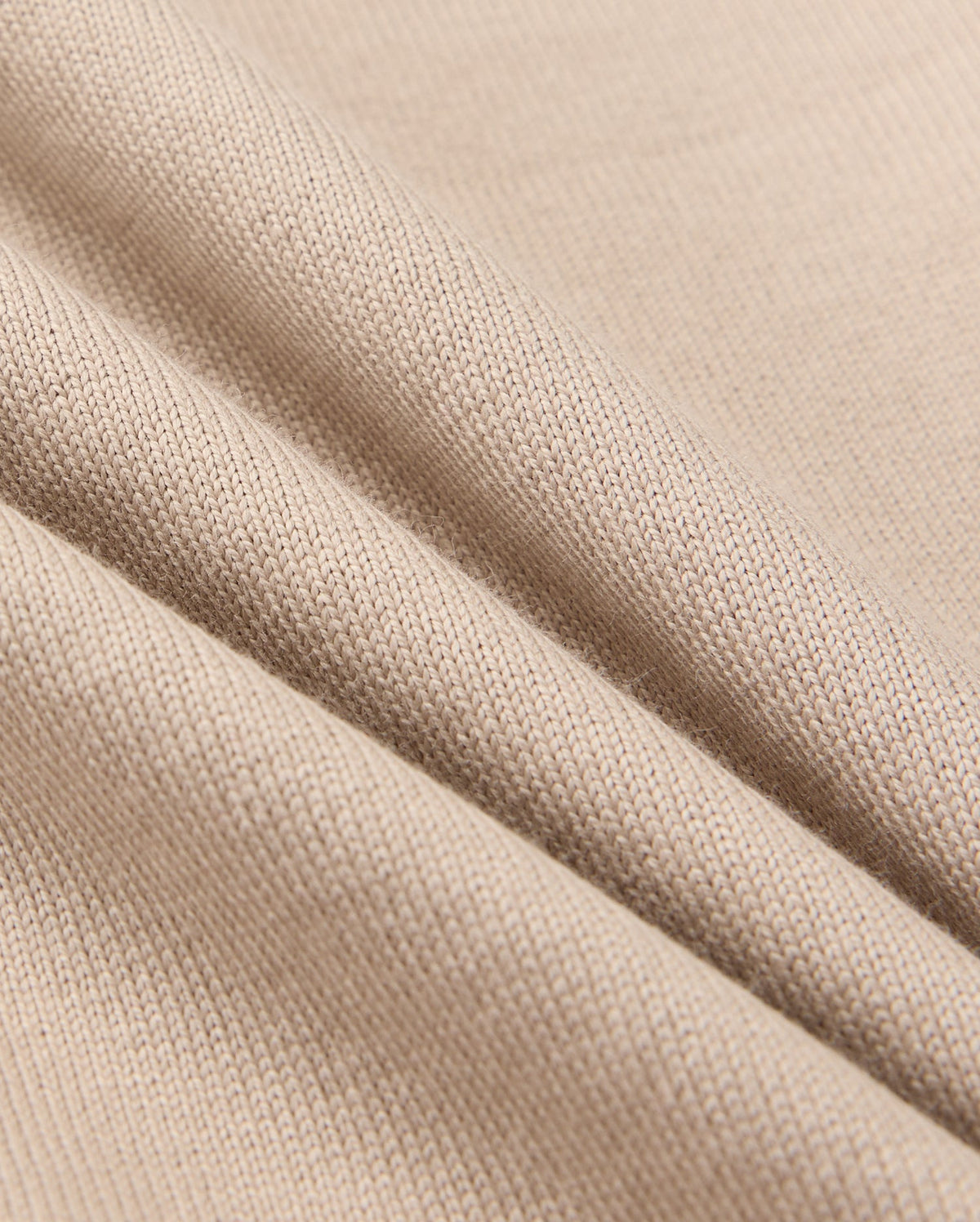 Close-up of beige fabric, showcasing a textured knit pattern with three soft folds that highlight its flexibility and smooth surface. The play of light and shadow defines the fine weave details, perfect for Psycho Bunny's KIDS MONROE HEAVY WEIGHT RELAXED FIT TEE, B0U910D200.