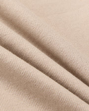 Close-up of beige fabric, showcasing a textured knit pattern with three soft folds that highlight its flexibility and smooth surface. The play of light and shadow defines the fine weave details, perfect for Psycho Bunny's KIDS MONROE HEAVY WEIGHT RELAXED FIT TEE, B0U910D200.