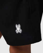Close-up of a black polyester mechanical stretch fabric with a small, white Psycho Bunny logo on the lower right side, symbolizing the KIDS MALTA HYDROCHROMIC SWIM TRUNK - B0W321B2SW.