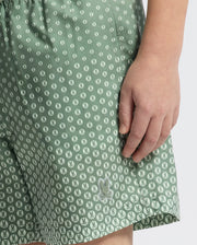 Close-up of a person wearing KIDS BENDIGO PRINTED SWIM TRUNK by Psycho Bunny, featuring a bunny pattern and small white dots, crafted from quick-dry fabric. The person's right hand rests by their side.