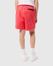 Rear view of a person wearing a white t-shirt, pink KIDS PARKER HYDROCHROMIC SWIM TRUNK - B0W646C200 by Psycho Bunny, white socks, and white shoes. The person is standing against a plain, light-colored background. The swim trunks feature an elastic waistband and a black back pocket on the right side.