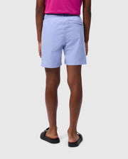  A person is standing with their back to the camera, wearing a bright pink shirt, **Psycho Bunny KIDS MELVIN SWIM TRUNK - B0W665C200** with quick-dry fabric, and black sandals. The background is plain and light-colored.