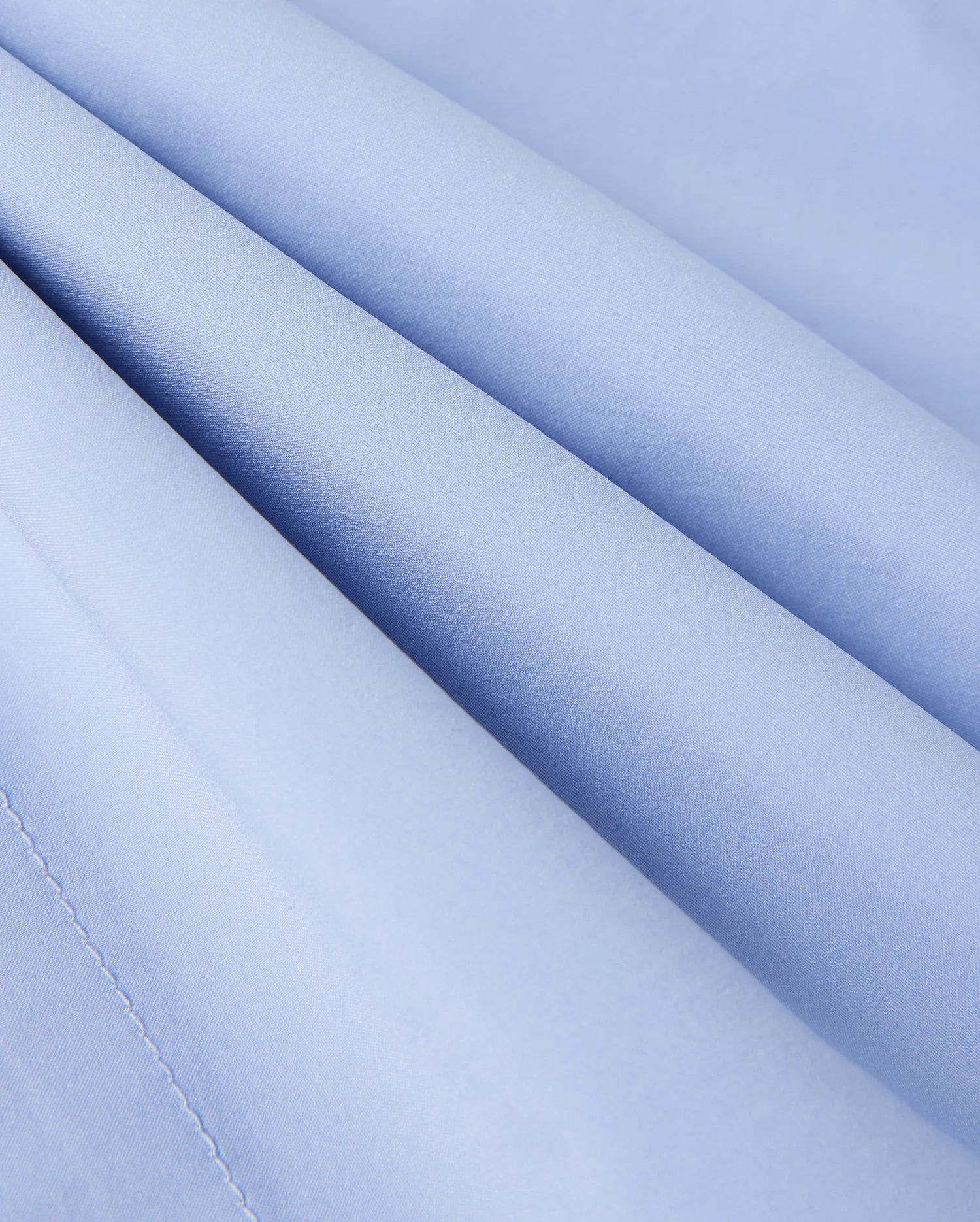 Close-up of Psycho Bunny's KIDS MELVIN SWIM TRUNK - B0W665C200: a light blue, quick-dry fabric with diagonal folds and a smooth, slightly shiny texture that creates wave-like patterns perfect for swimwear.