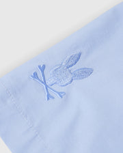 Close-up of the KIDS MELVIN SWIM TRUNK by Psycho Bunny in light blue, showcasing an embroidered rabbit head and crossbones in matching thread. The quick-dry fabric's stitching is detailed, smooth, and well-tailored. Model: B0W665C200.