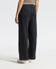 A person wearing stylish Psycho Bunny WOMENS ALEXANDER SWEATPANT - B2P157E200 and white sneakers is standing with their back facing the camera against a plain, light-colored background.