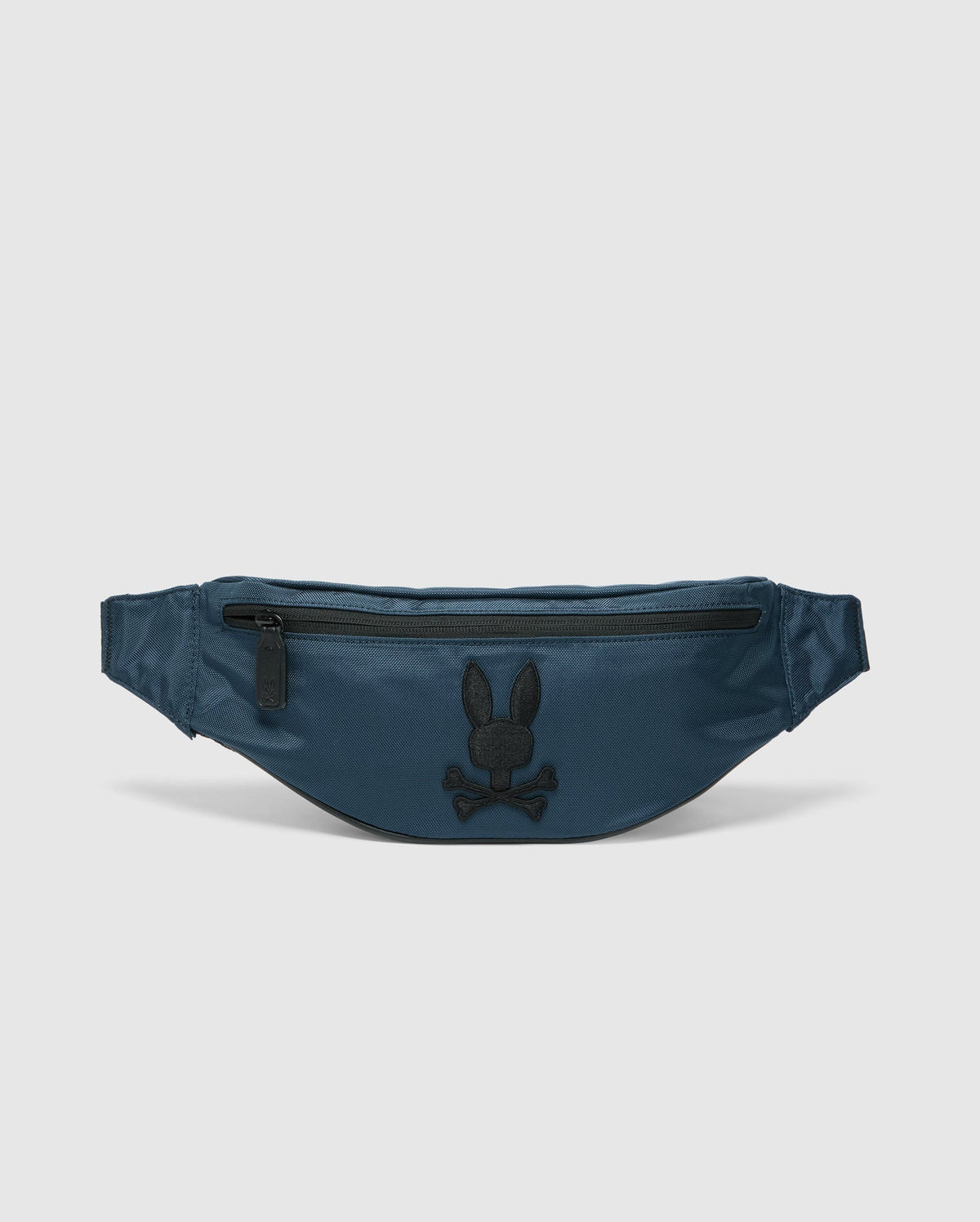 The Psycho Bunny MENS CROSS BODY BAG - B6A181E200, crafted from blue nylon, features a black zipper and an embroidered rabbit head logo above crossed bones in black on the front, making it the perfect functional waist bag for men.