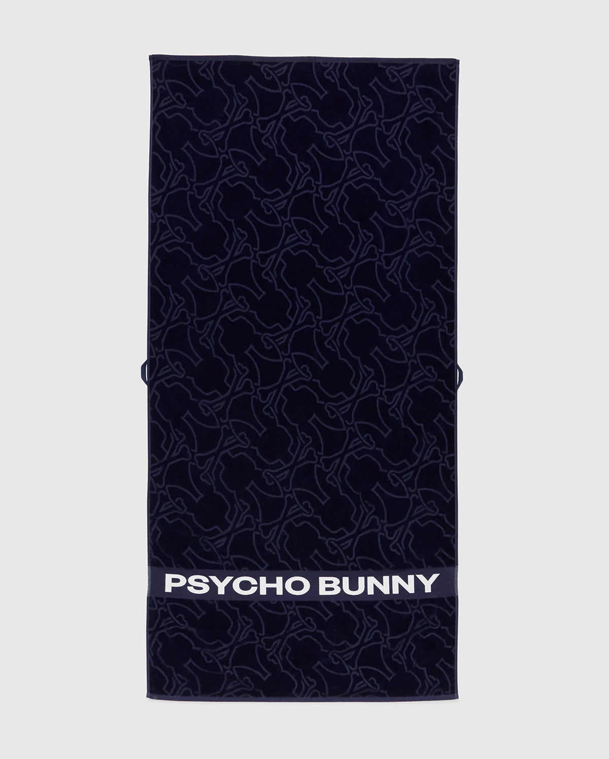 The Towel - B6A287F200 by Psycho Bunny is a rectangular dark towel made from premium terrycloth cotton, featuring an intricate bunny pattern. The bottom displays "PSYCHO BUNNY" in bold white letters, showcasing high-quality design.