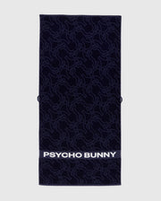 The Towel - B6A287F200 by Psycho Bunny is a rectangular dark towel made from premium terrycloth cotton, featuring an intricate bunny pattern. The bottom displays "PSYCHO BUNNY" in bold white letters, showcasing high-quality design.