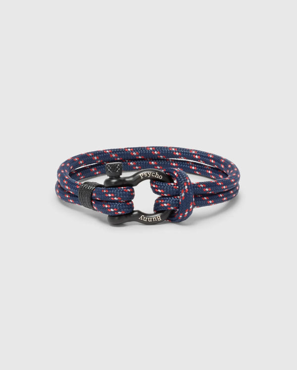 The Psycho Bunny MEN'S ROPE BRACELET - B6A368E200 features a chic braided nylon design in navy and red with metal accents and engraved text. Its circular coil on a plain background makes it a modern, must-have accessory for any man's wardrobe.