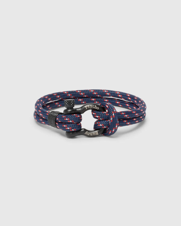 The Psycho Bunny MEN'S ROPE BRACELET - B6A368E200 features a chic braided nylon design in navy and red with metal accents and engraved text. Its circular coil on a plain background makes it a modern, must-have accessory for any man's wardrobe.