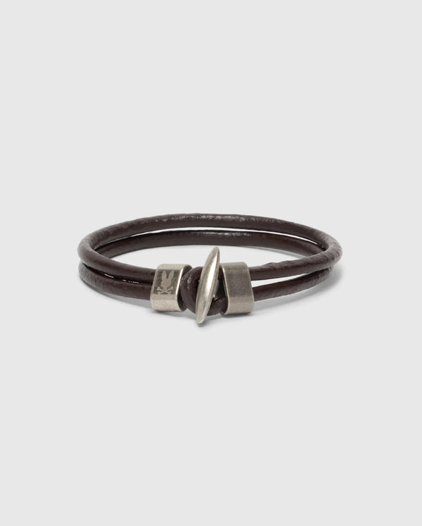 The Psycho Bunny MEN'S LEATHER BRACELET - B6A369E200 is a stylish double-wrap piece with a sleek cylindrical metal clasp, elegantly presented on a plain white background. The clasp adds modern flair to the rich dark brown leather, perfect for any style-conscious individual.