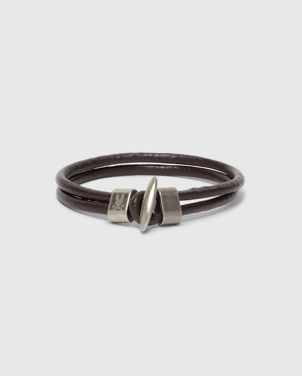The Psycho Bunny MEN'S LEATHER BRACELET - B6A369E200 is a stylish double-wrap piece with a sleek cylindrical metal clasp, elegantly presented on a plain white background. The clasp adds modern flair to the rich dark brown leather, perfect for any style-conscious individual.
