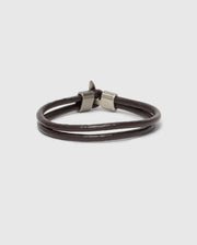 The Psycho Bunny Men's Leather Bracelet - B6A369E200 showcases a double band in brown leather with sleek metallic clasps. Perfect for a modern fit, it is elegantly presented on a plain gray background, emphasizing its timeless appeal.