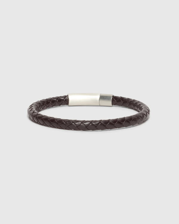 A stylish and elegant accessory, the MEN'S BRAIDED LEATHER BRACELET - B6A371E200 from Psycho Bunny showcases a sophisticated dark brown braided leather design with a sleek polished silver clasp, set against a minimalist light gray backdrop.