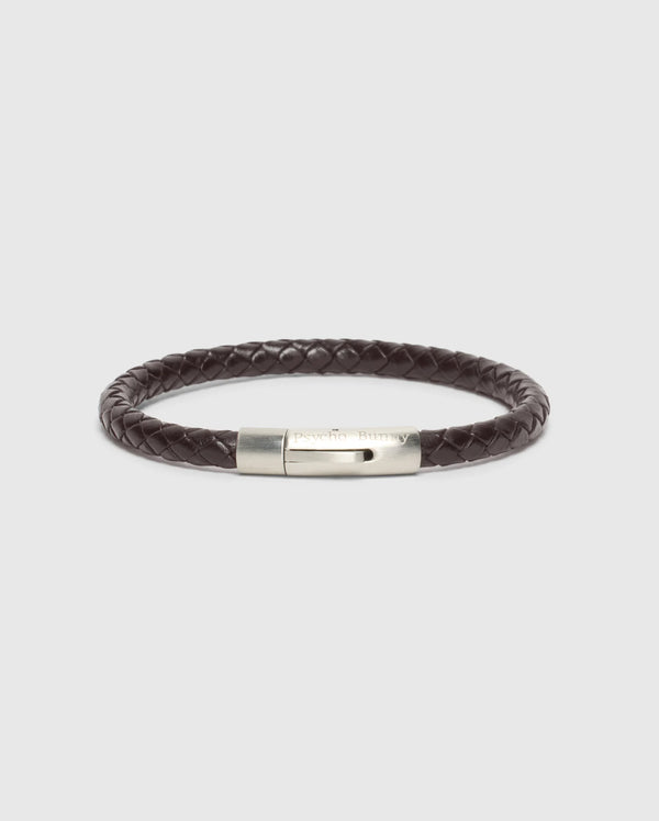 A classy statement piece, the MEN'S BRAIDED LEATHER BRACELET - B6A371E200 by Psycho Bunny features a dark brown braided leather design with a silver clasp, elegantly showcased against a plain white background.