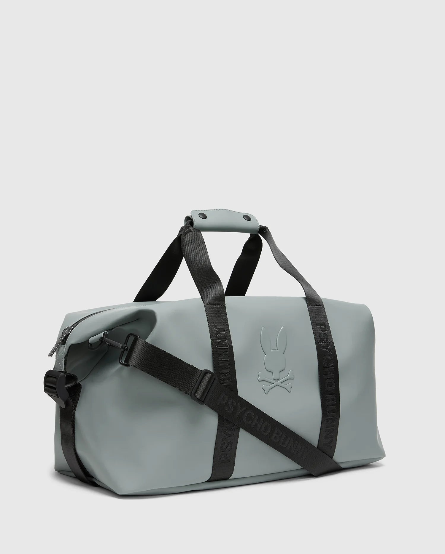 The Psycho Bunny Men's Duffle Bag (B6A472F200) is a gray carry-all with black adjustable straps and handles, featuring an embossed stylized bunny with crossbones. The straps display "PSYCHO BUNNY" boldly, complementing its minimalist design. Ideal for efficient packing on the move.