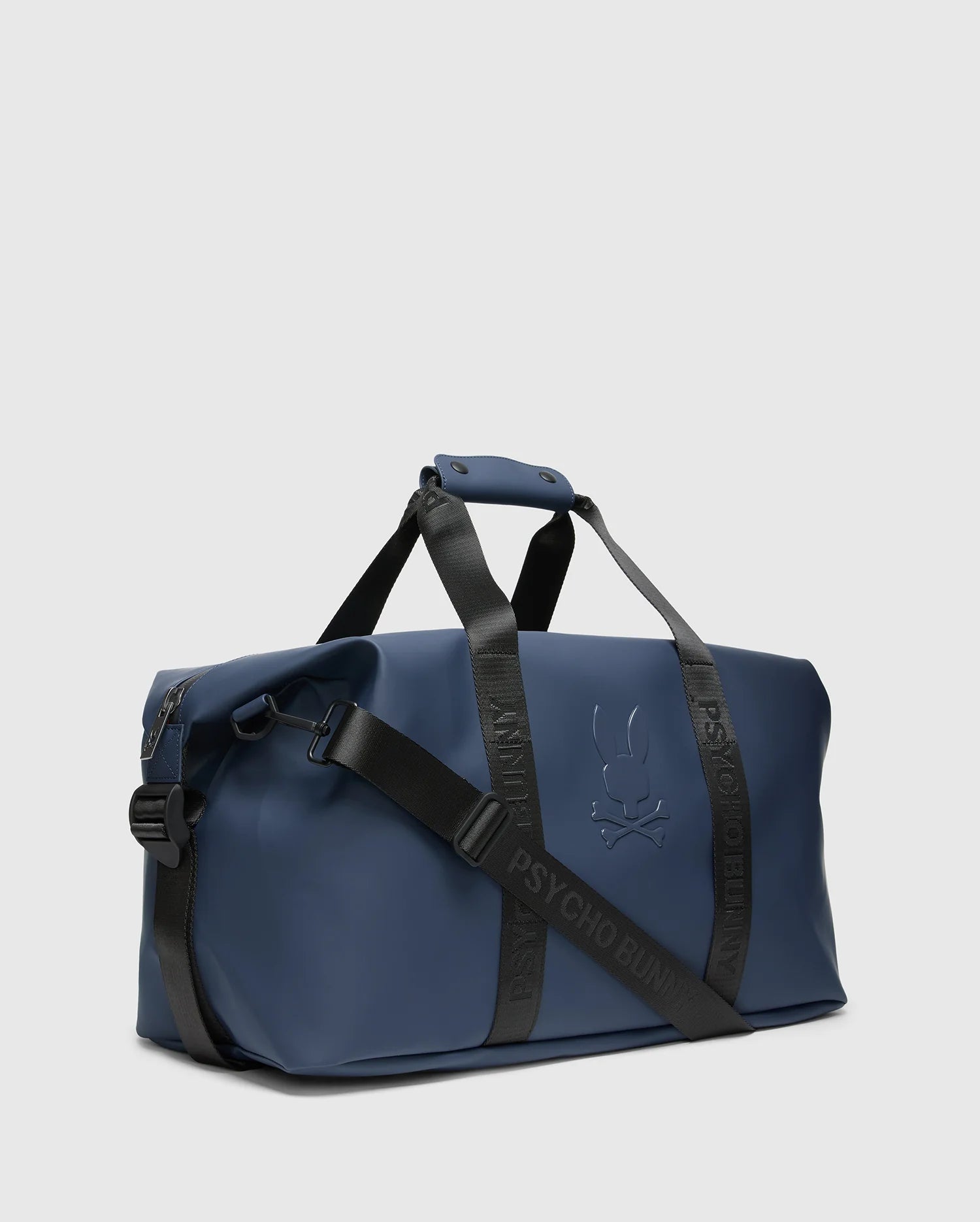 The Psycho Bunny MENS DUFFLE BAG - B6A472F200 is a quality blue bag with black straps, featuring the brand's logo and name embossed. Designed for travel, it offers a structured form, top handle, and adjustable shoulder strap against a plain background.