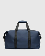 A sleek, blue mens duffle bag (B6A472F200) from Psycho Bunny sits against a gray backdrop. It features black handles and shoulder strap, with "PSYCHO BUNNY" emblazoned on the quality handles.