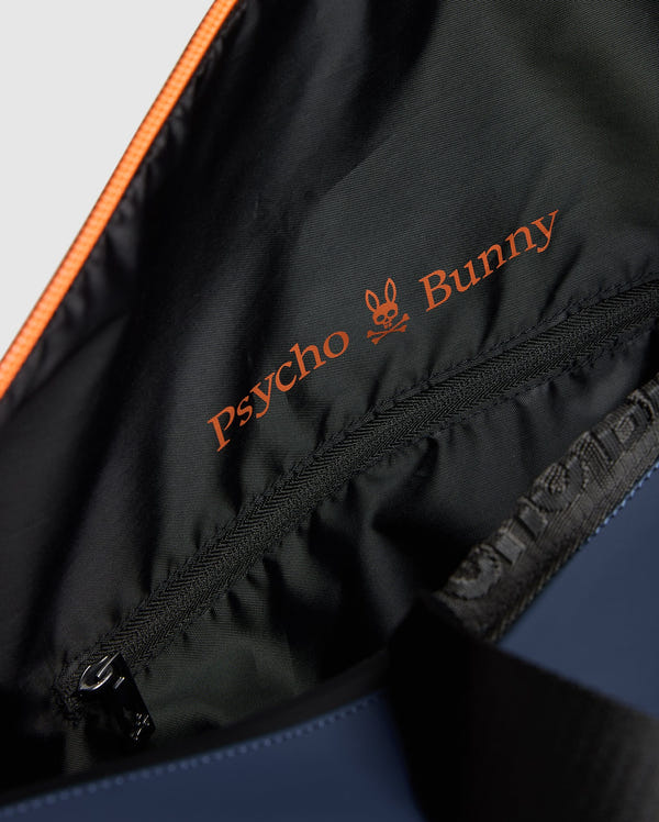 A close-up of the MENS DUFFLE BAG - B6A472F200 reveals the vibrant orange embroidered "Psycho Bunny" logo on its black lining, adorned with a stylish bunny skull design. A gleaming zipper adds a touch of quality craftsmanship.