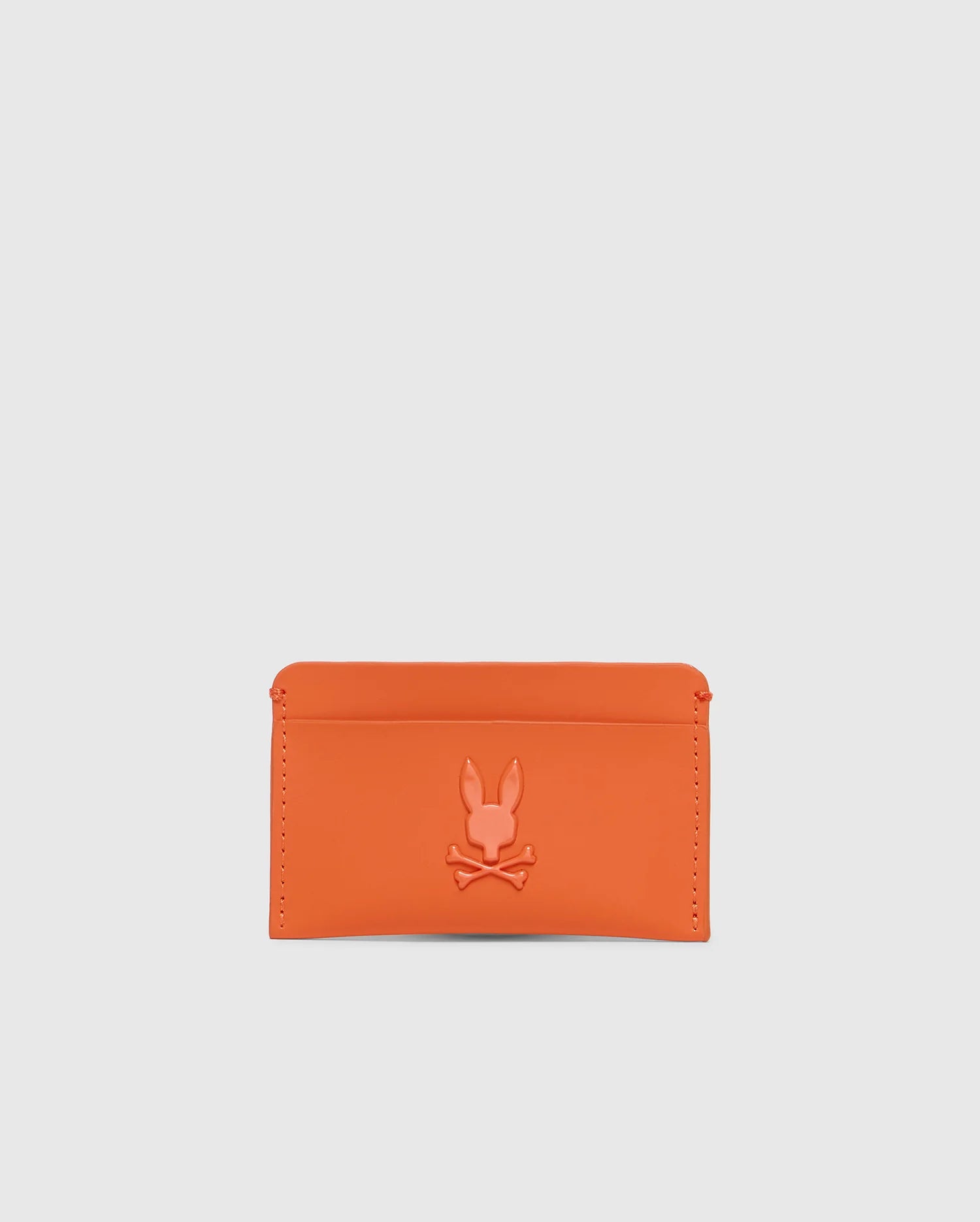 The Psycho Bunny Men's Rubberized Card Case (B6A473F200) in orange features a rabbit and crossbones design embossed on durable polyester. This minimalist card case is stylish, practical, and perfect for safely carrying essentials against a plain white background.