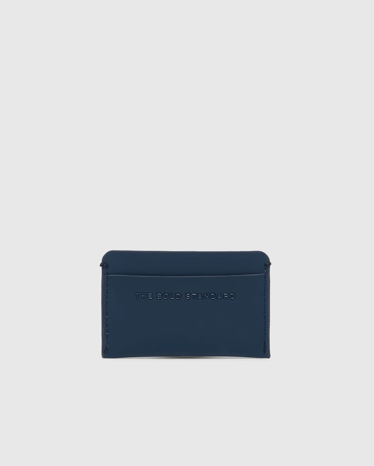 A minimalist, small, dark blue card holder embossed with "The Bold Standard," the Psycho Bunny MENS RUBBERIZED CARD CASE - B6A473F200 ensures peace of mind and safety for your essentials, elegantly displayed against a plain white background.