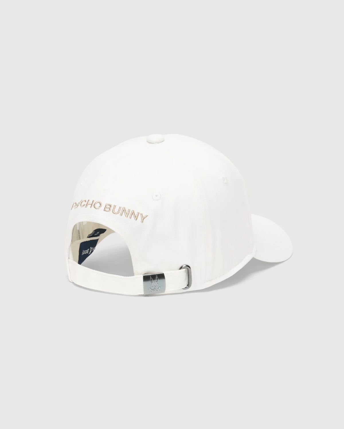 The Men's New Castle Graphic Baseball Cap by Psycho Bunny features white cotton twill, an adjustable strap with a metal buckle at the back, "PSYCHO BUNNY" embroidered in pink on the back panel for a luxurious touch, and a small logo tag near the buckle.