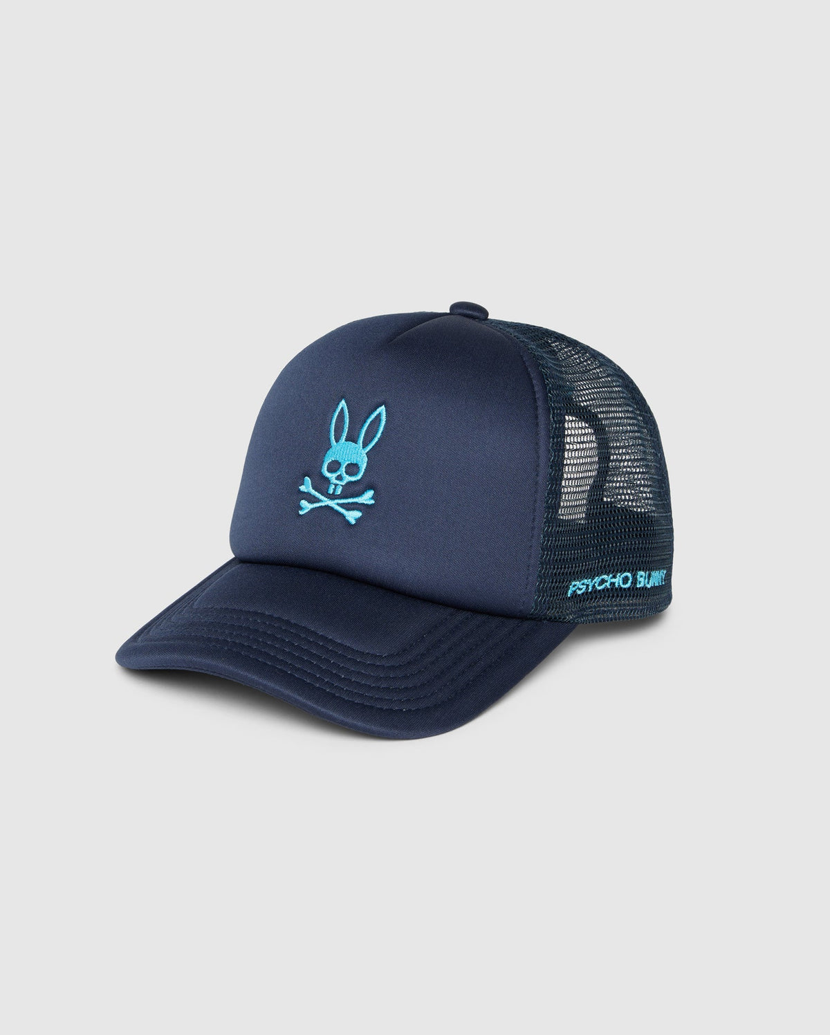 A navy blue **MENS PARIS TRUCKER CAP - B6A591C200** with a light blue bunny skull and crossbones logo on the front. The words "**Psycho Bunny**" are printed in light blue on the side. The cap boasts mesh paneling at the back and a curved brim for a classic look.