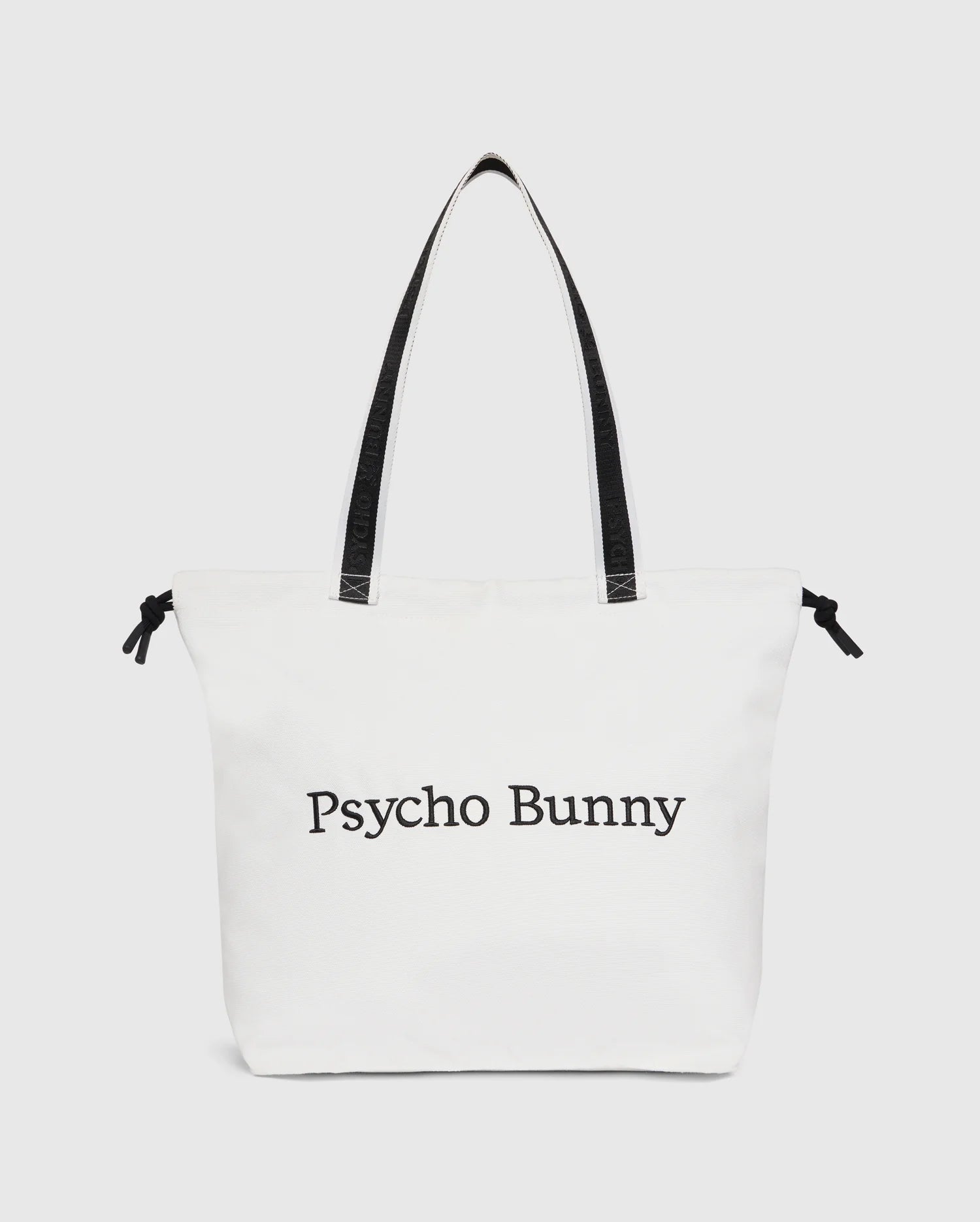 The Psycho Bunny TENNIS TOTE - B6A596C200 is a white canvas tote bag with black handles, featuring the text "Psycho Bunny" on the front. It effortlessly combines style and functionality, making it perfect for tennis enthusiasts.