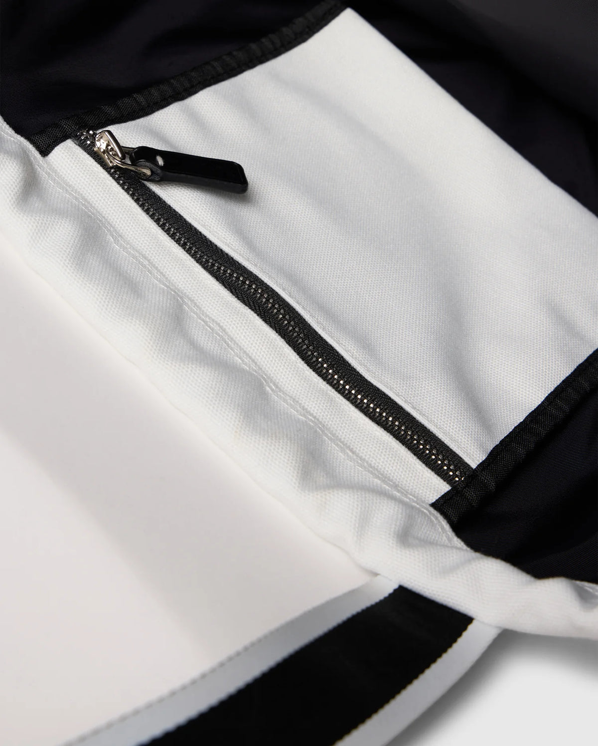 Close-up of the Psycho Bunny TENNIS TOTE - B6A596C200 shows a black and white garment with a zippered pocket. The contrast stitching between canvas sections highlights the design, while an embroidered logo adds elegance and seamlessly blends into its sophisticated style.