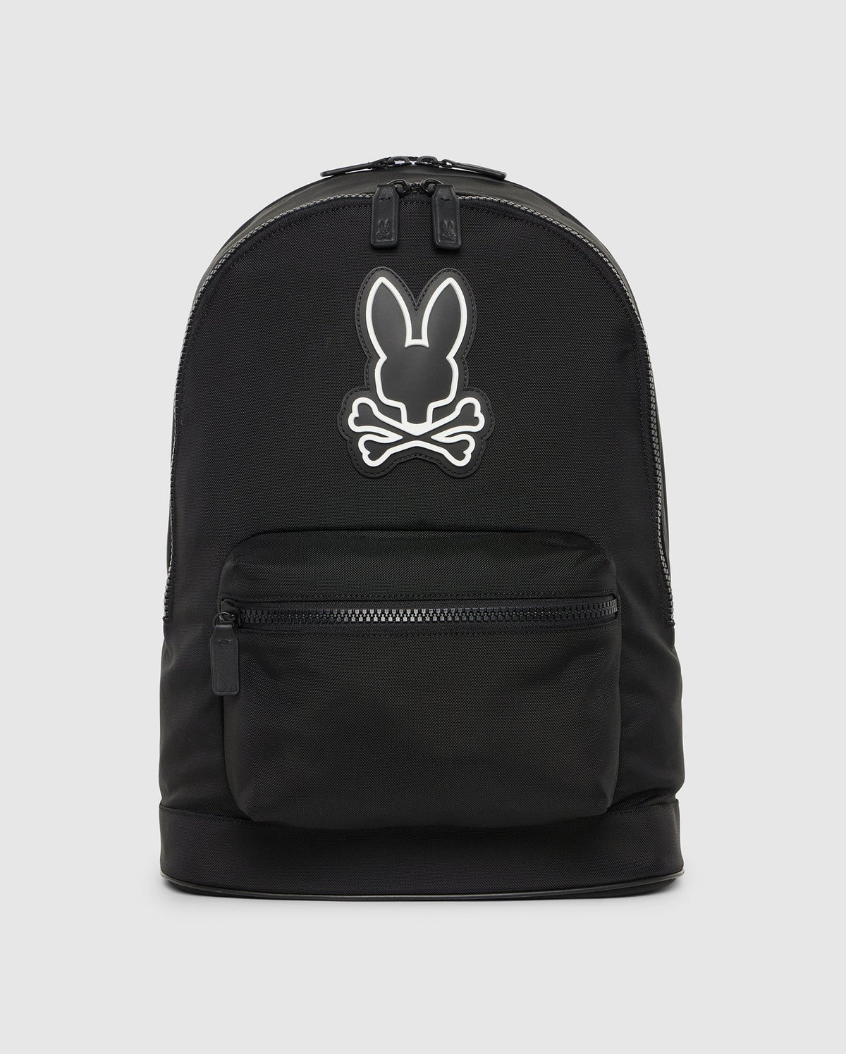 A black canvas backpack with leather trimmings, featuring a white outline of a stylized rabbit head logo on its upper half, with a small external zippered pocket at the front. Product Name: DOME BACKPACK - B6A628Z1BP by Psycho Bunny