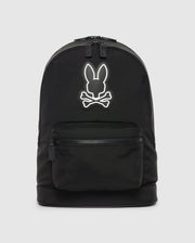 A black canvas backpack with leather trimmings, featuring a white outline of a stylized rabbit head logo on its upper half, with a small external zippered pocket at the front. Product Name: DOME BACKPACK - B6A628Z1BP by Psycho Bunny