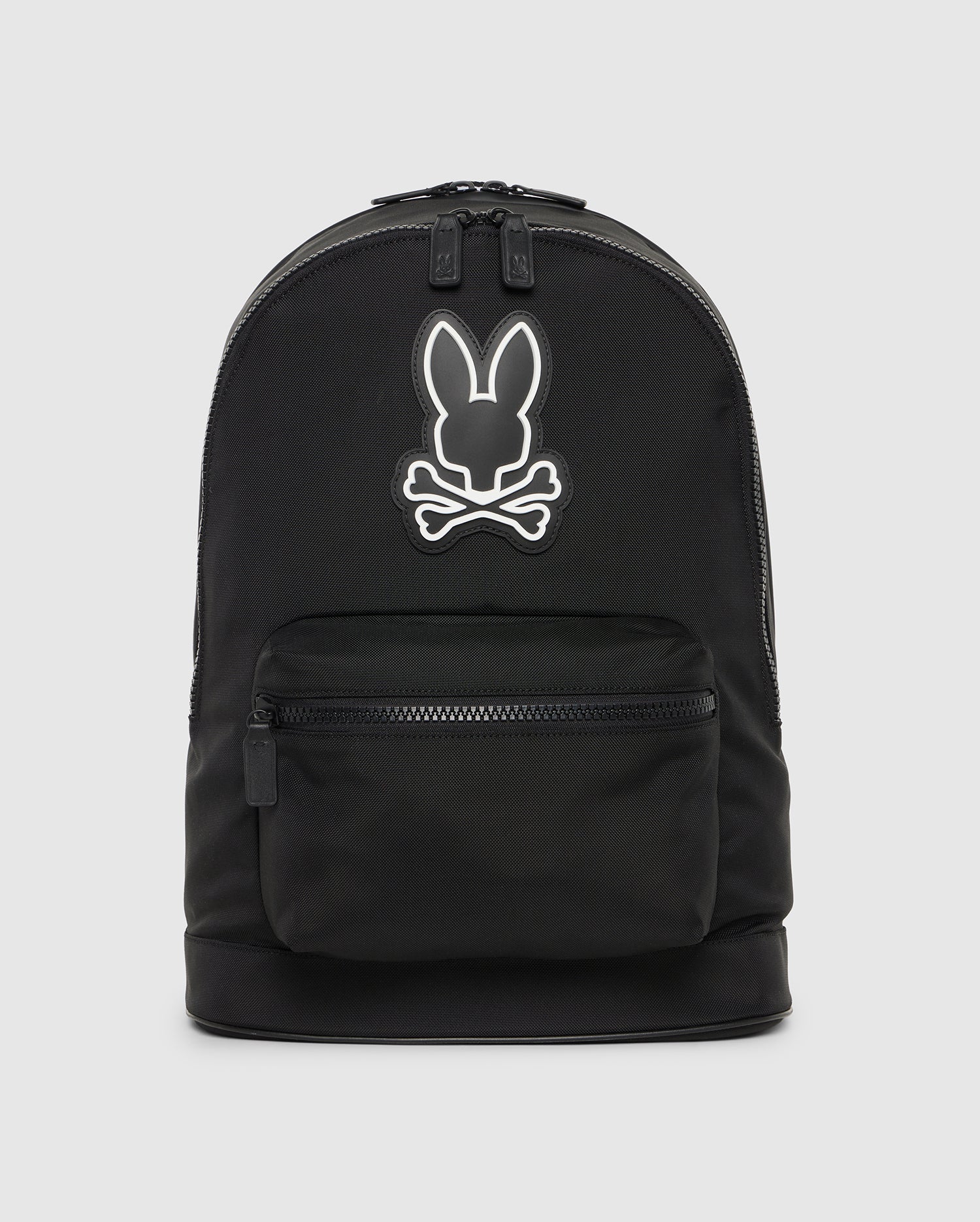A black canvas backpack with leather trimmings, featuring a white outline of a stylized rabbit head logo on its upper half, with a small external zippered pocket at the front. Product Name: DOME BACKPACK - B6A628Z1BP by Psycho Bunny