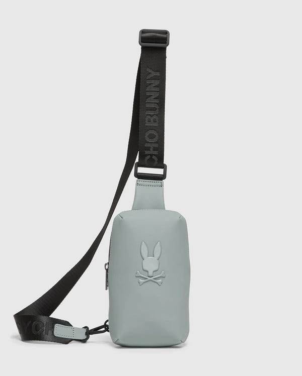 The MENS RUBBERIZED CROSSBODY - B6A635F200 by Psycho Bunny is a durable, pastel green bag made of sturdy polyester with a black adjustable strap. It features an embossed bunny with crossed bones logo and the strap boldly displays "PSYCHO BUNNY" in black letters.