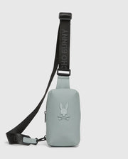 The MENS RUBBERIZED CROSSBODY - B6A635F200 by Psycho Bunny is a durable, pastel green bag made of sturdy polyester with a black adjustable strap. It features an embossed bunny with crossed bones logo and the strap boldly displays "PSYCHO BUNNY" in black letters.