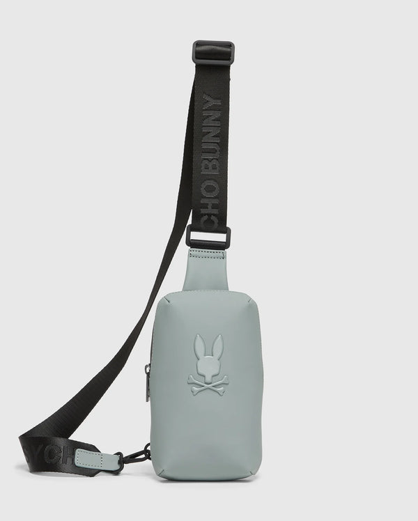 The MENS RUBBERIZED CROSSBODY - B6A635F200 by Psycho Bunny is a durable, pastel green bag made of sturdy polyester with a black adjustable strap. It features an embossed bunny with crossed bones logo and the strap boldly displays "PSYCHO BUNNY" in black letters.