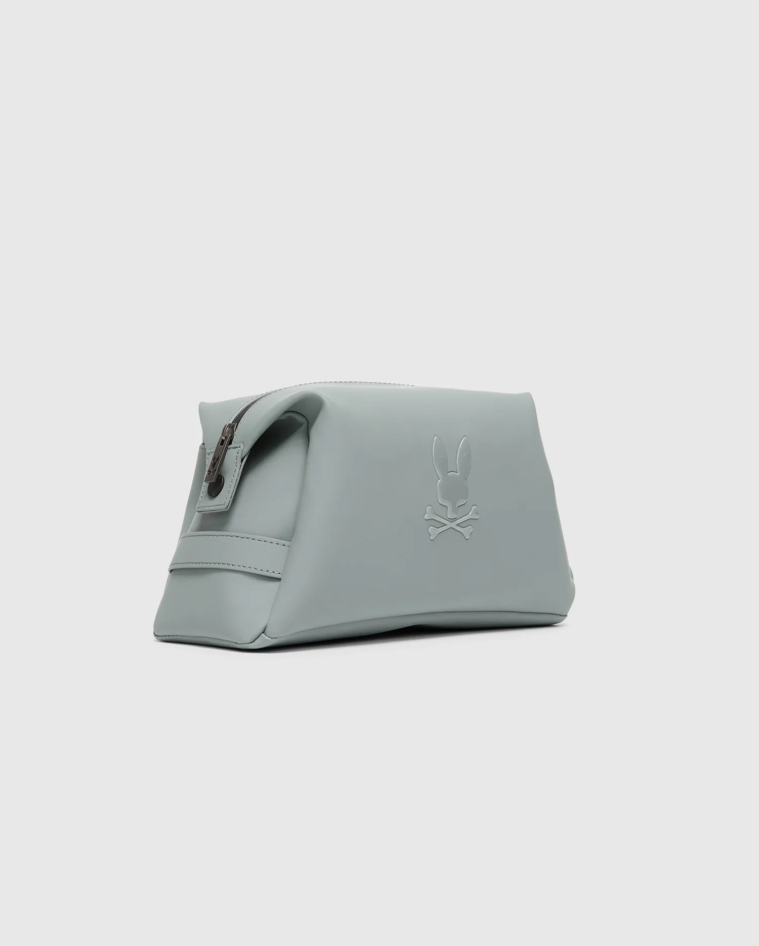 The Psycho Bunny MENS TOILETRY KIT - B6A636F200 is a minimalist light gray polyester pouch, ideal for organizing essentials on the go. It features a zippered top and an embossed bunny and crossbones design on the side, enhancing its sleek and modern look against the plain gray background.