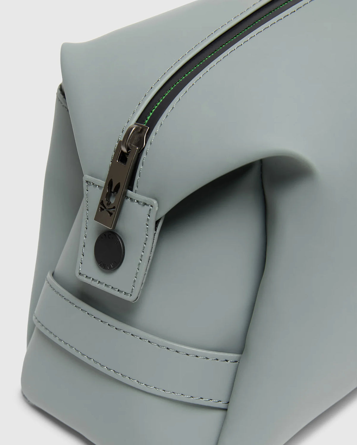Close-up of the Psycho Bunny MENS TOILETRY KIT - B6A636F200, a light gray, rectangular polyester bag with clean stitching and minimalist design, ideal for organizing essentials. It features a partially open zipper with metal pull and small leather tab.