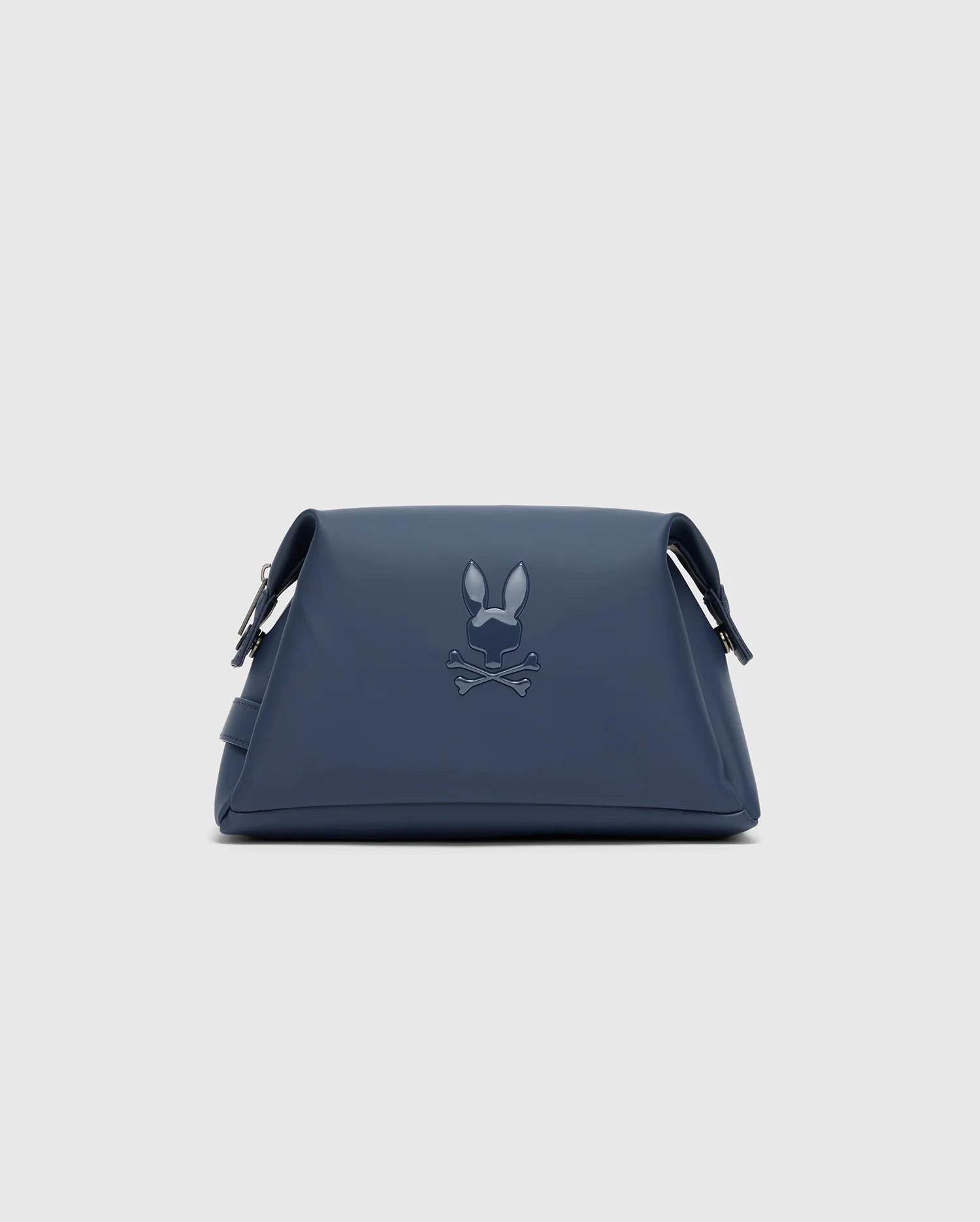 The Psycho Bunny MENS TOILETRY KIT - B6A636F200 is a navy blue triangular bag with an embossed rabbit ears and crossed bones design. Made from 100% polyester, it has adjustable straps and a minimalist style, ideal for organizing essentials on the go.
