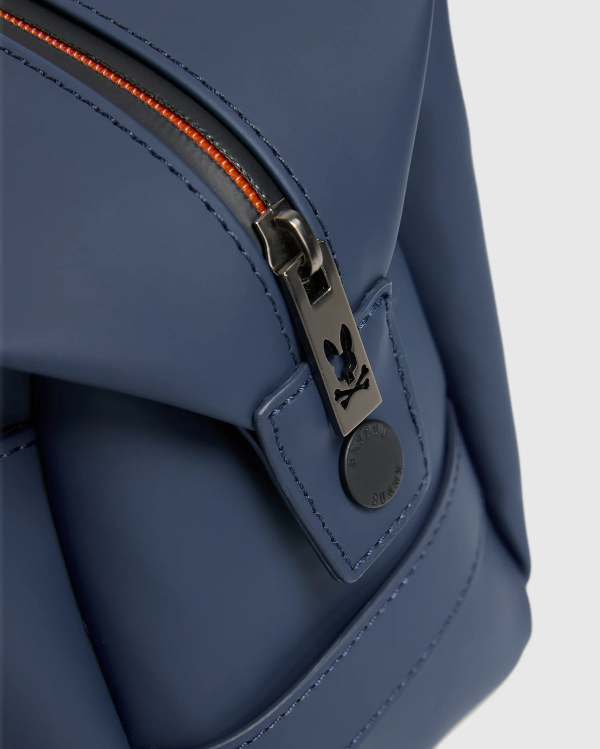 Close-up of the Psycho Bunny MENS TOILETRY KIT - B6A636F200 in blue, crafted from 100% polyester. It features a black zipper with orange teeth, equipped with a round black pull tab adorned with a small rabbit logo to keep your essentials organized on the go.
