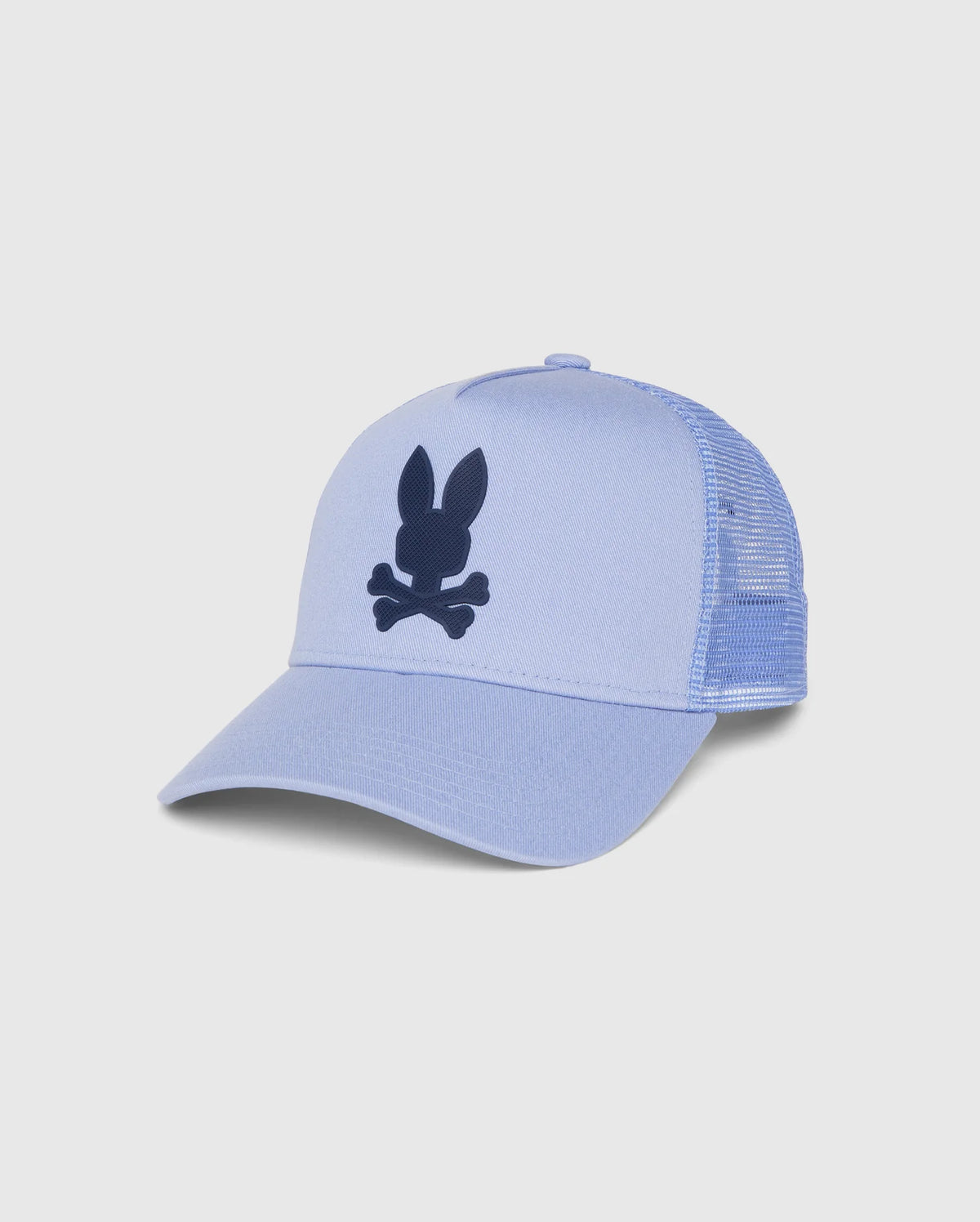 A light blue MENS RIVIERA TRUCKER CAP - B6A667C200 with a mesh back and a solid front panel. The front features a black graphic of a bunny head with crossbones beneath it, capturing early 2000s nostalgia. The cap has a curved brim and an adjustable snapback fastening at the back by Psycho Bunny.