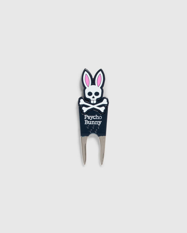 Image of a DIVOT TOOL - B6A699C200 from Psycho Bunny with a design featuring a skull with bunny ears and the text "Psycho Bunny" underneath. The tool has two prongs at the bottom, and the skull and ears are in black, white, and pink. A perfect addition to golf gifts, this tool also comes with a magnetic ball marker. The background is plain gray.