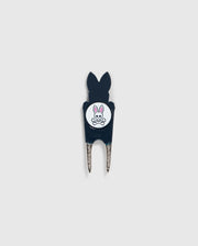 A Psycho Bunny DIVOT TOOL - B6A699C200 featuring a black handle with a white circular logo. The logo shows an illustration of a bunny head with crossed bones underneath. The two prongs of the tool are metal, and it includes a magnetic ball marker. Ideal for those seeking unique golf gifts.
