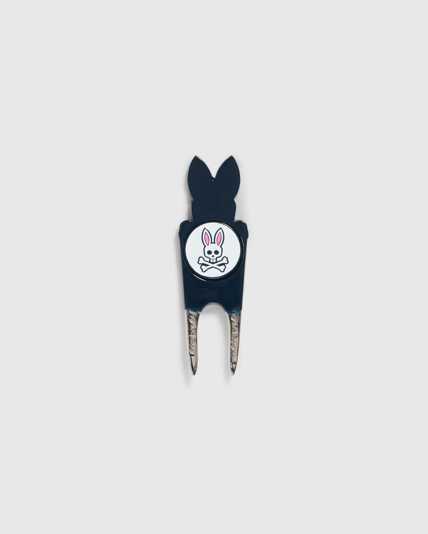 A Psycho Bunny DIVOT TOOL - B6A699C200 featuring a black handle with a white circular logo. The logo shows an illustration of a bunny head with crossed bones underneath. The two prongs of the tool are metal, and it includes a magnetic ball marker. Ideal for those seeking unique golf gifts.